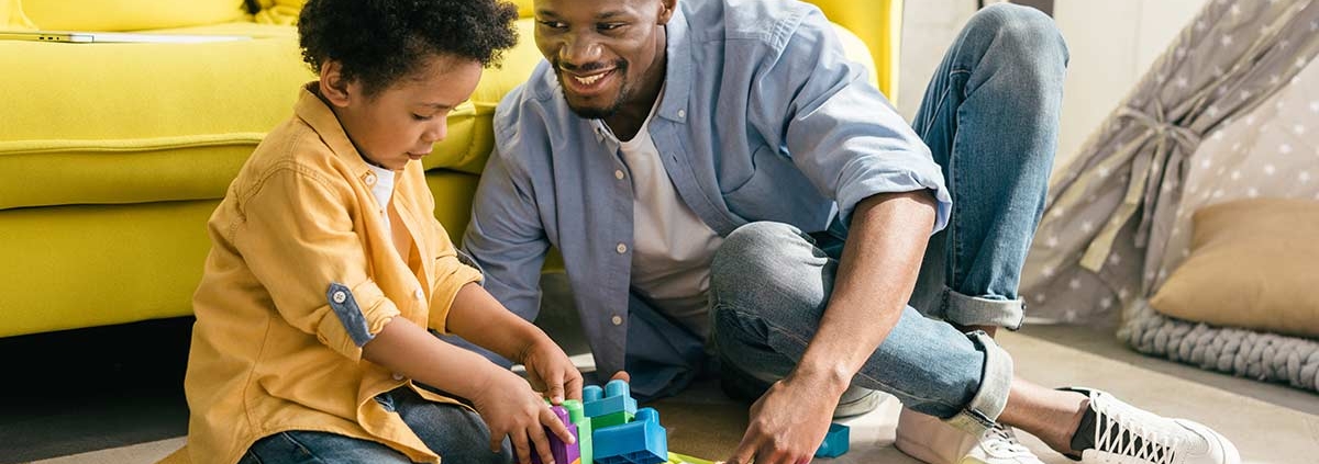 Vater und Sohn sitzen vor gelbem Sofa auf dem Boden und spielen mit Bauklötzen - Scheidungsimmobilie