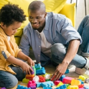 Vater und Sohn sitzen vor gelbem Sofa auf dem Boden und spielen mit Bauklötzen - Scheidungsimmobilie