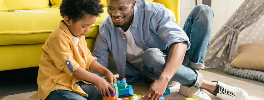 Vater und Sohn sitzen vor gelbem Sofa auf dem Boden und spielen mit Bauklötzen - Scheidungsimmobilie
