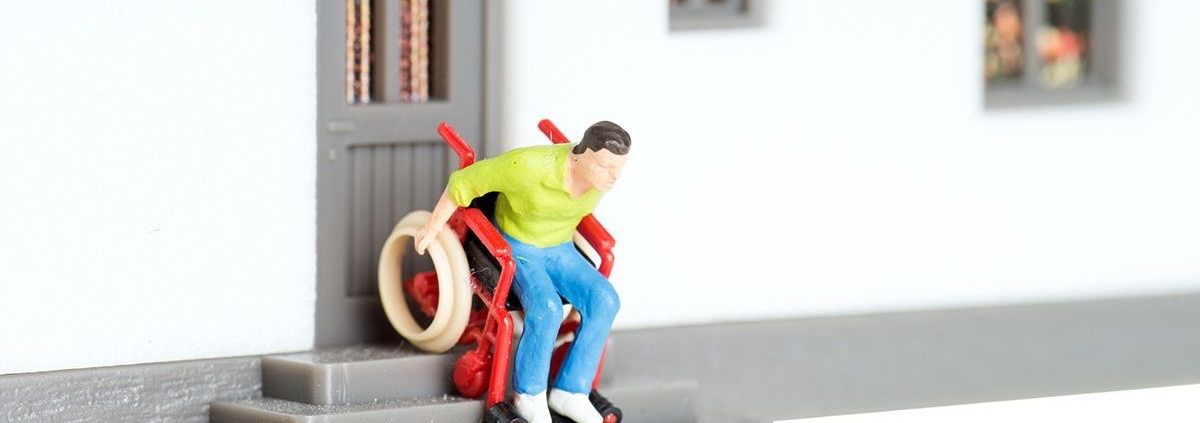 Ein Spielzeugmann in einem Rollstuhl fährt eine Spielzeugtreppe herunter - Wohnen im Alter