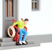 Ein Spielzeugmann in einem Rollstuhl fährt eine Spielzeugtreppe herunter - Wohnen im Alter