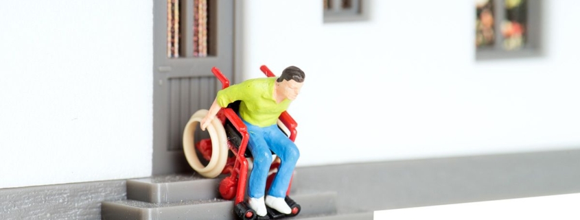 Ein Spielzeugmann in einem Rollstuhl fährt eine Spielzeugtreppe herunter - Wohnen im Alter
