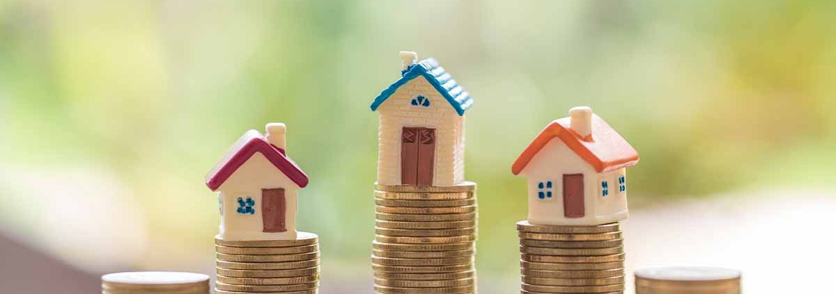 Drei Modellhäuschen stehen auf Stapeln von Münzen - Immobilienfinanzierung