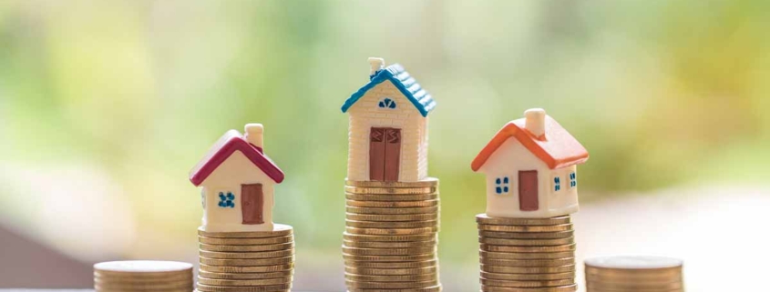 Drei Modellhäuschen stehen auf Stapeln von Münzen - Immobilienfinanzierung