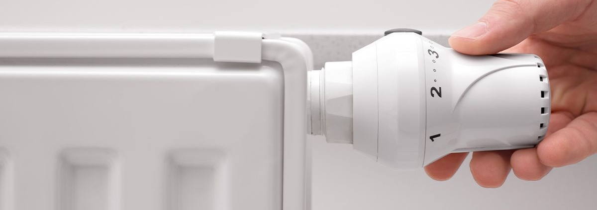 Eine Hand dreht an einer Heizung vor einer weißen Wand - Energie sparen für Eigentümer