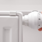Eine Hand dreht an einer Heizung vor einer weißen Wand - Energie sparen für Eigentümer