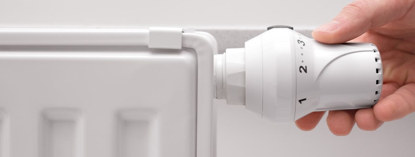 Eine Hand dreht an einer Heizung vor einer weißen Wand - Energie sparen für Eigentümer
