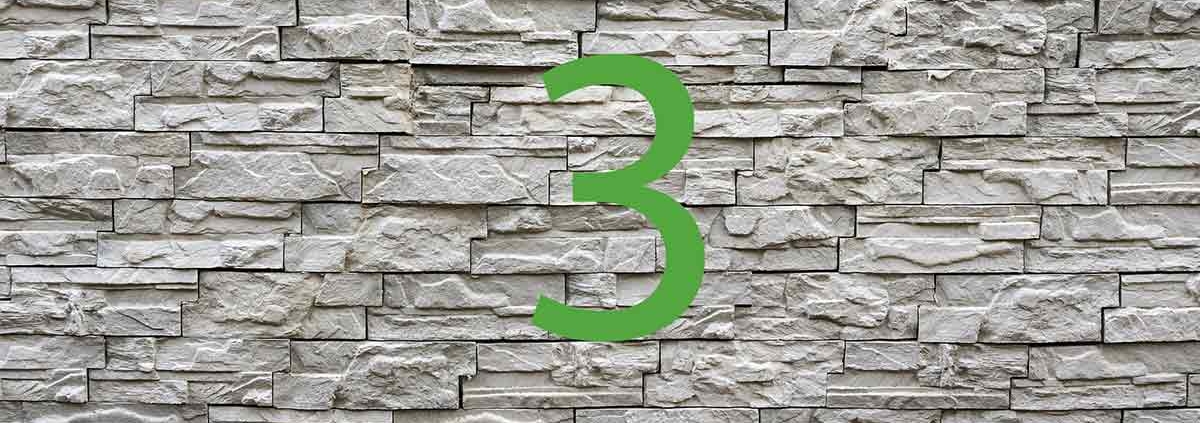 Vor einer Steinmauer steht eine grüne 3 | Haus aus dem 3D-Drucker