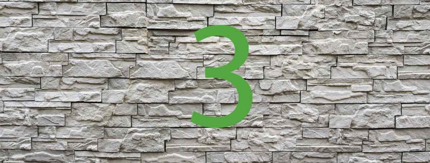 Vor einer Steinmauer steht eine grüne 3 | Haus aus dem 3D-Drucker