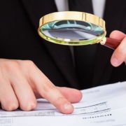 Zwei Hände mit einer Lupe die Dokumente in einem Ordner zeigen - Nachlassverzeichnis Erbimmobilien