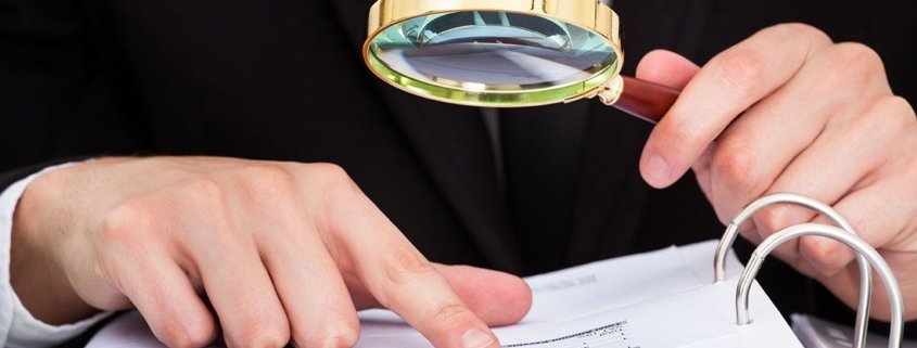 Zwei Hände mit einer Lupe die Dokumente in einem Ordner zeigen - Nachlassverzeichnis Erbimmobilien