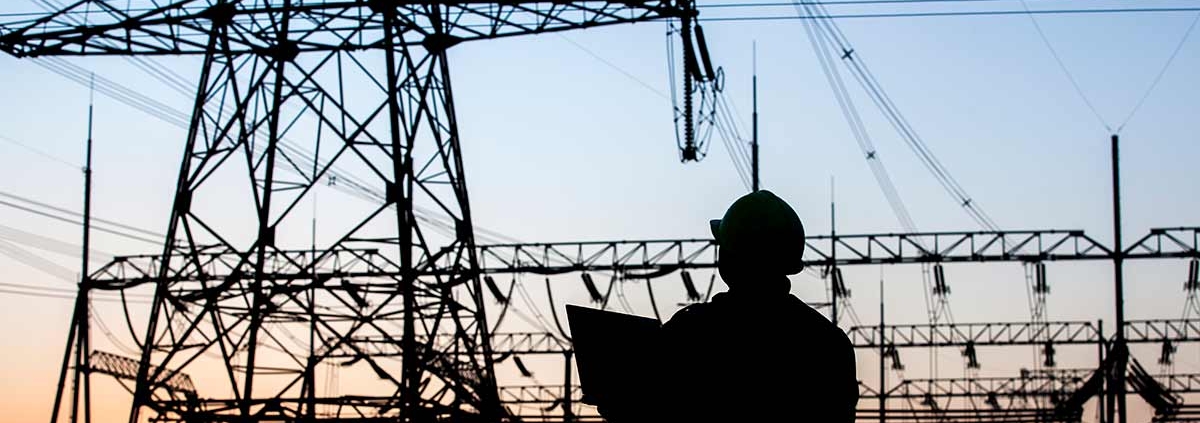 Ein Mann vor Strommasten im Sonnenuntergang - Strompreise- lohnt sich der Wechsel