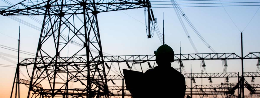 Ein Mann vor Strommasten im Sonnenuntergang - Strompreise- lohnt sich der Wechsel