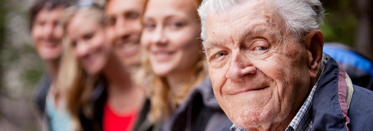 Alter Mann sitzt mit seinen Kindern und Enkeln draußen.