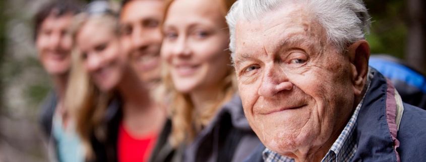 Alter Mann sitzt mit seinen Kindern und Enkeln draußen.
