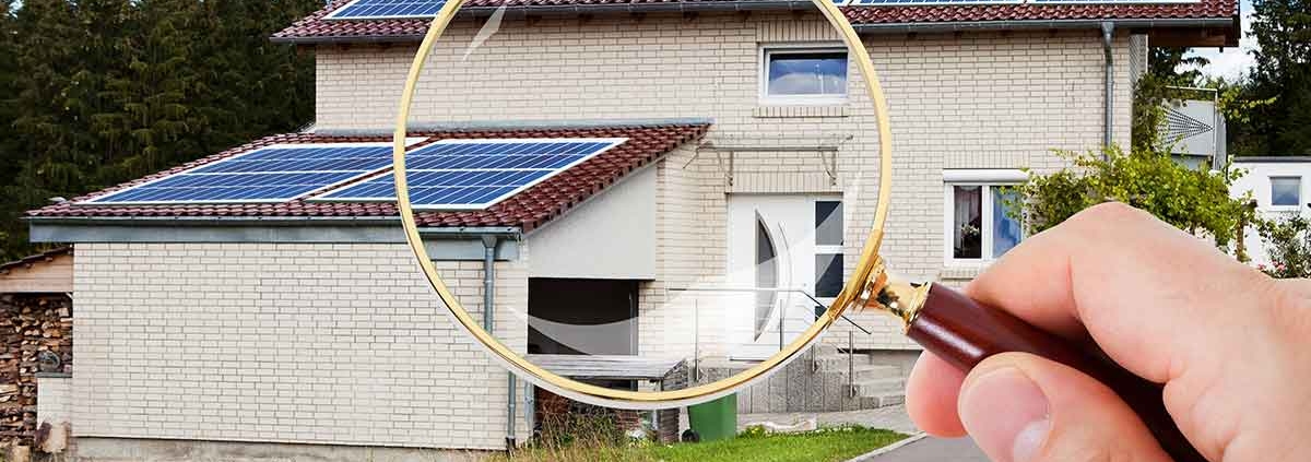 Eine Hand mit Lupe vor einem Haus mit Garage - Suchauftrag