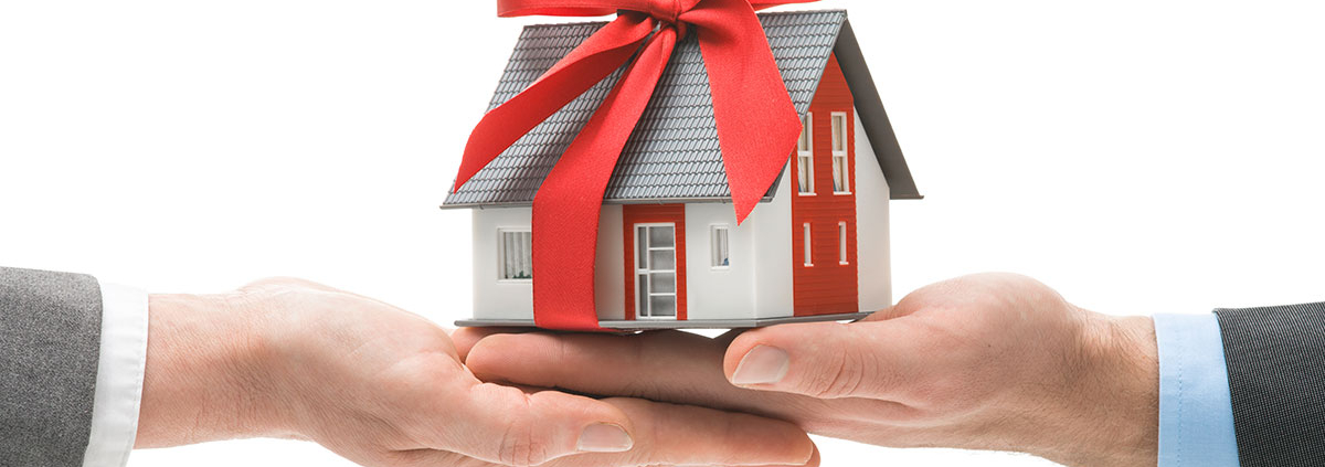 Ein Miniaturhaus mit Schleife und zwei Händen - Schenkung