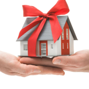 Ein Miniaturhaus mit Schleife und zwei Händen - Schenkung