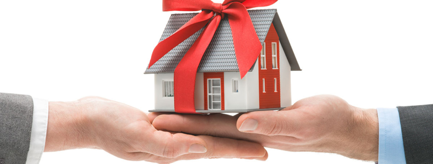 Ein Miniaturhaus mit Schleife und zwei Händen - Schenkung