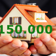 Ein paar Hände halten ein Spielzeughaus mit der Zahl 150000 - Kfw Zuschuss