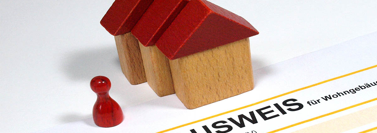 Drei Spielzeughäuser und eine Figur und ein Energieausweis - Sanierungspflicht EU