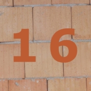 Orange Zahl 16 auf gemauerter Häuserwand.