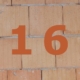 Orange Zahl 16 auf gemauerter Häuserwand.