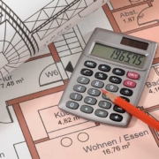 Auf dem Grundrissplan einer Immobilie liegen ein weiterer zusammengerollter Grundrissplan, ein Taschenrechner und ein Stift | Immobilienfinanzierung