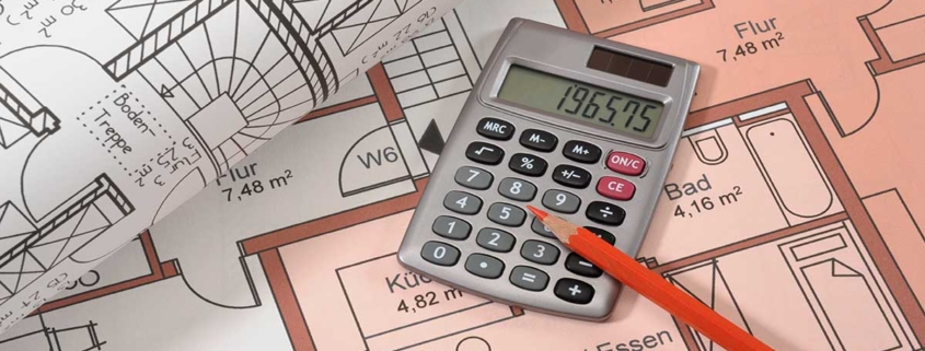 Auf dem Grundrissplan einer Immobilie liegen ein weiterer zusammengerollter Grundrissplan, ein Taschenrechner und ein Stift | Immobilienfinanzierung