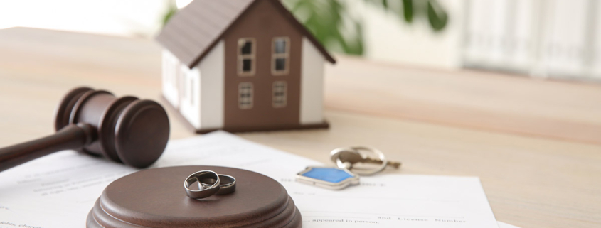 Richterhammer, mit Eheringen und Papieren auf einem Tisch, dahinter ein Modellhaus und Schlüssel; Teilungsversteigerung